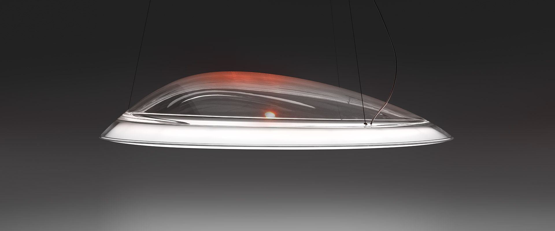 Artemide Ameluna pendant lamp: sleek oval transparent diffuser with warm red-orange inner glow and white LED ring, suspended by thin cables