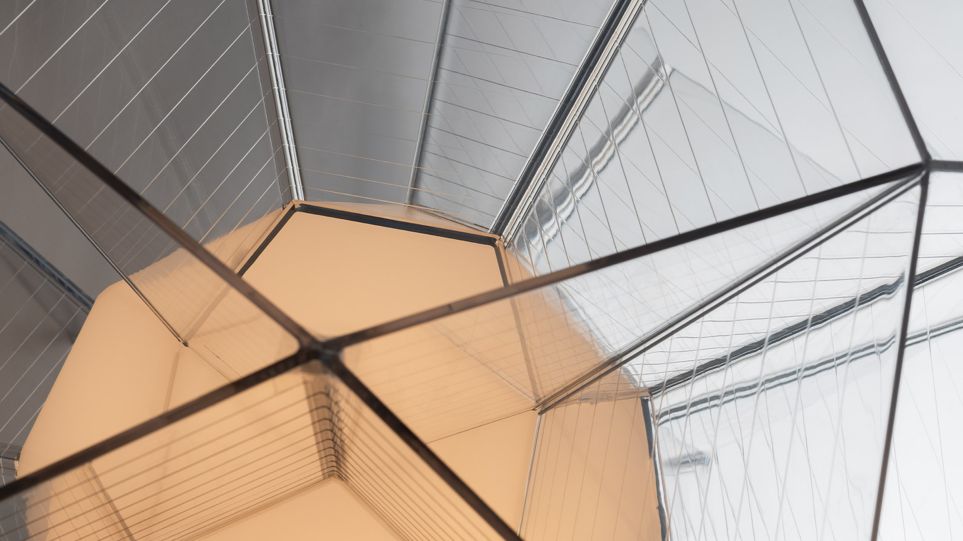 Close-up interior view of Arctic pendant lamp: geometric mirrored facets with black metal frame, warm amber and silver reflective panels