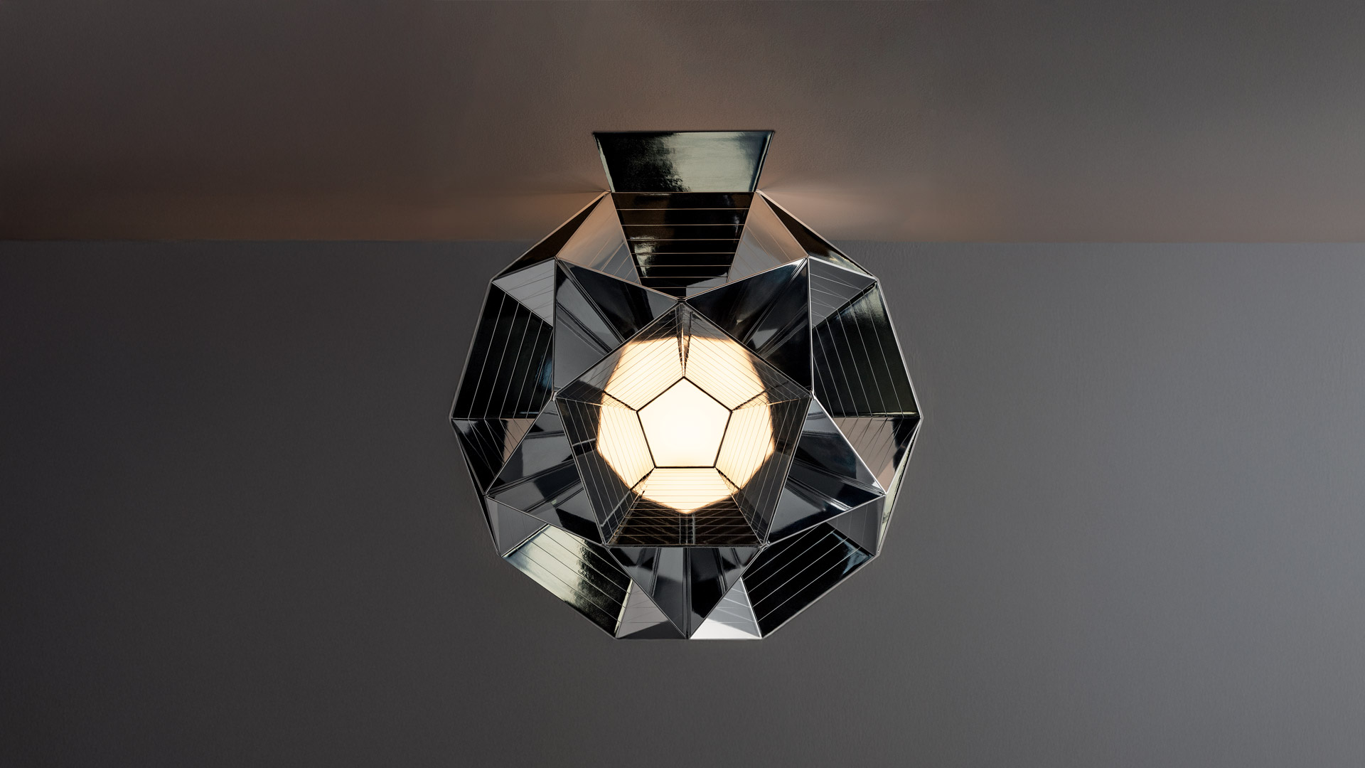Upward view of two geometric faceted glass towers with warm golden light reflecting on angular panels against a grey sky