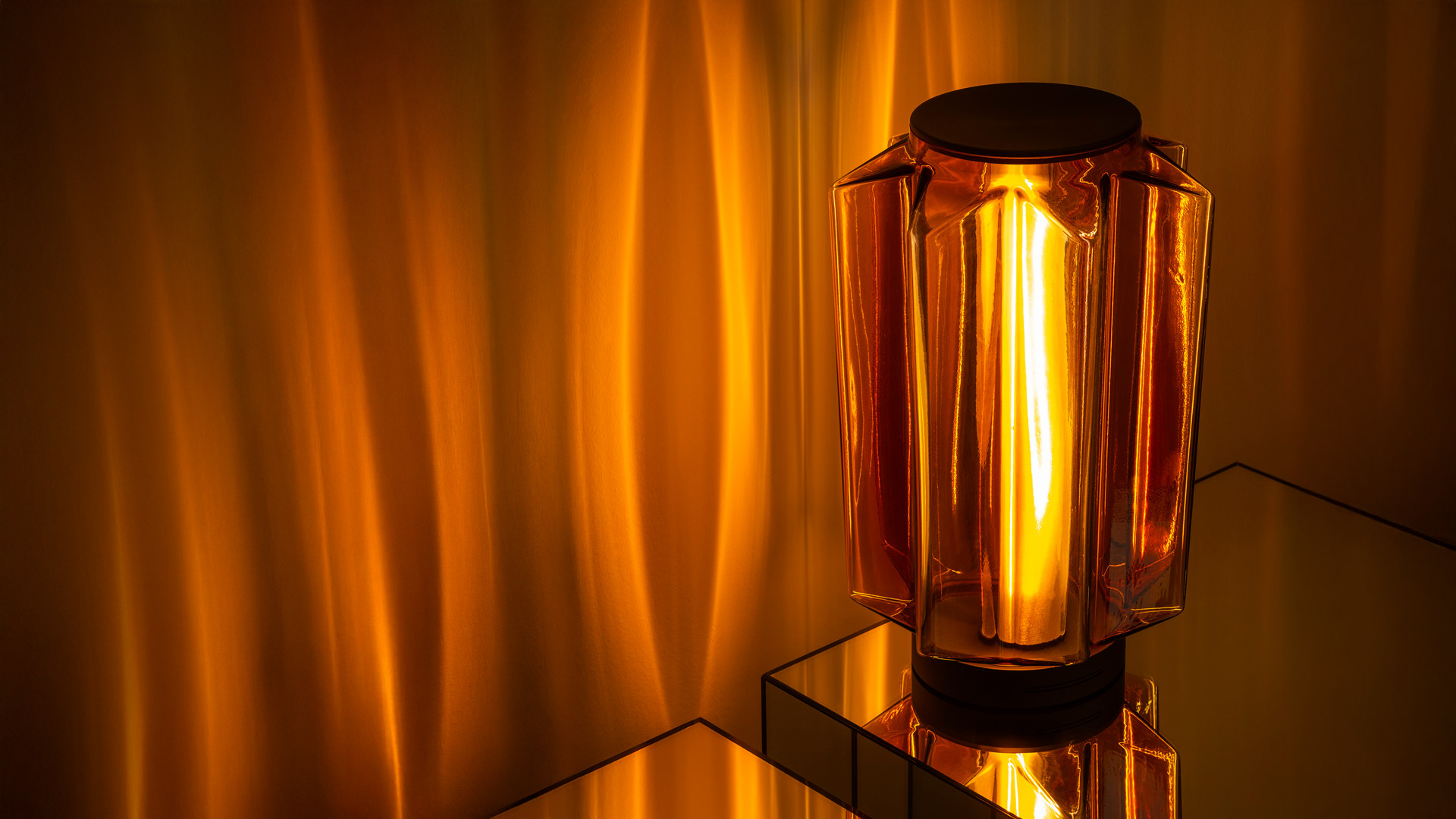 Auralia table lamp by Artemide: amber glass geometric diffuser with visible filament bulb casting warm golden light on surrounding surfaces