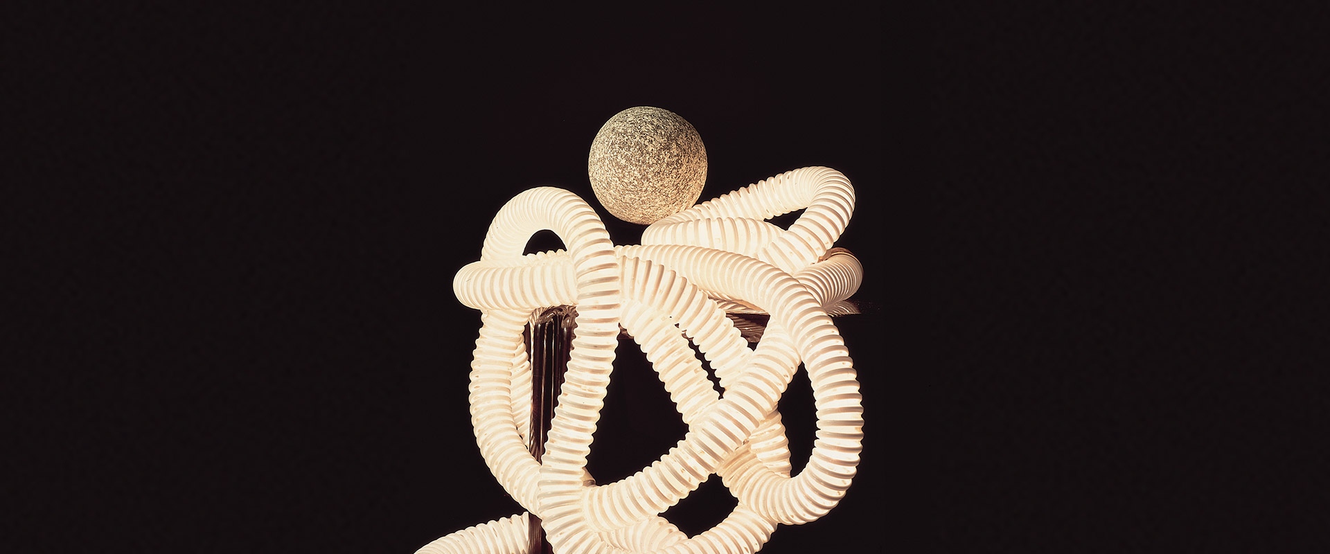 Boalum lamp by Artemide: flexible tubular white structure intertwined in organic shapes with a textured sphere on top, on black background