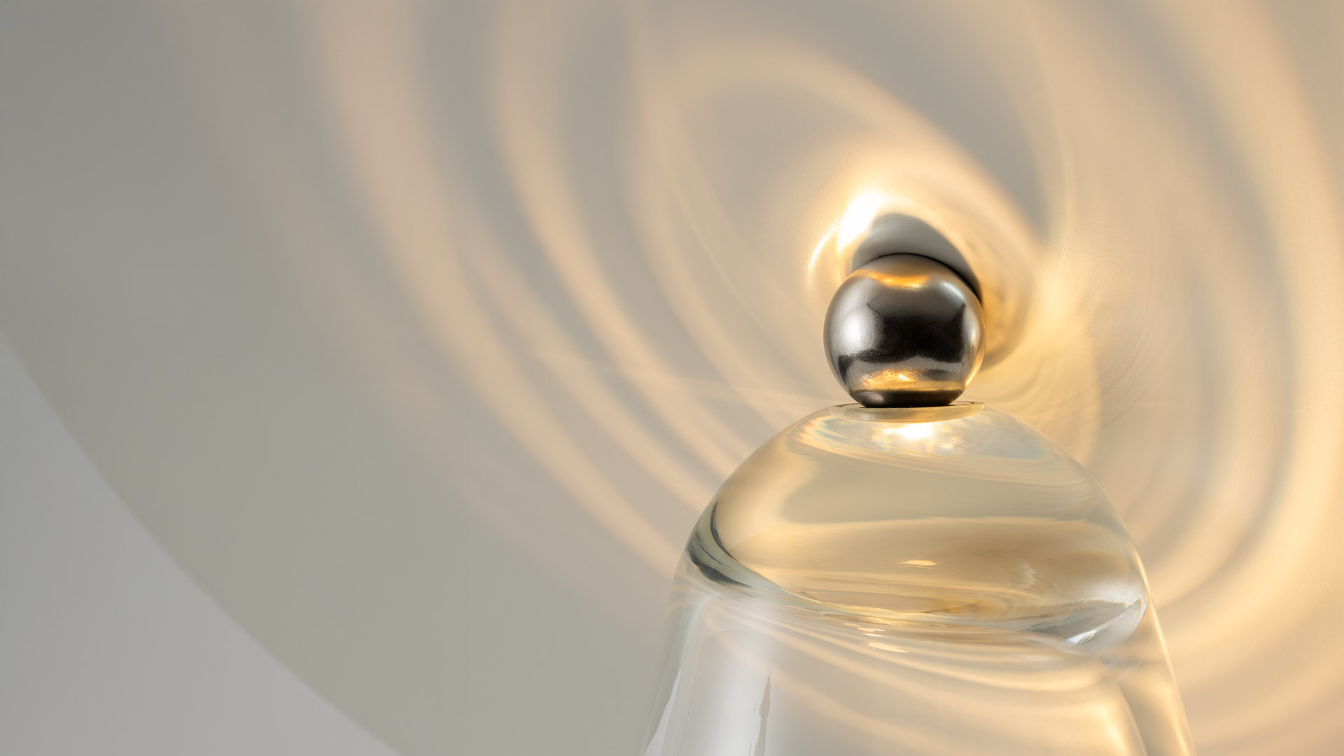 Artemide table lamp with tilted golden disc reflector on a clear glass cone base, casting warm spiral light on a marble surface.