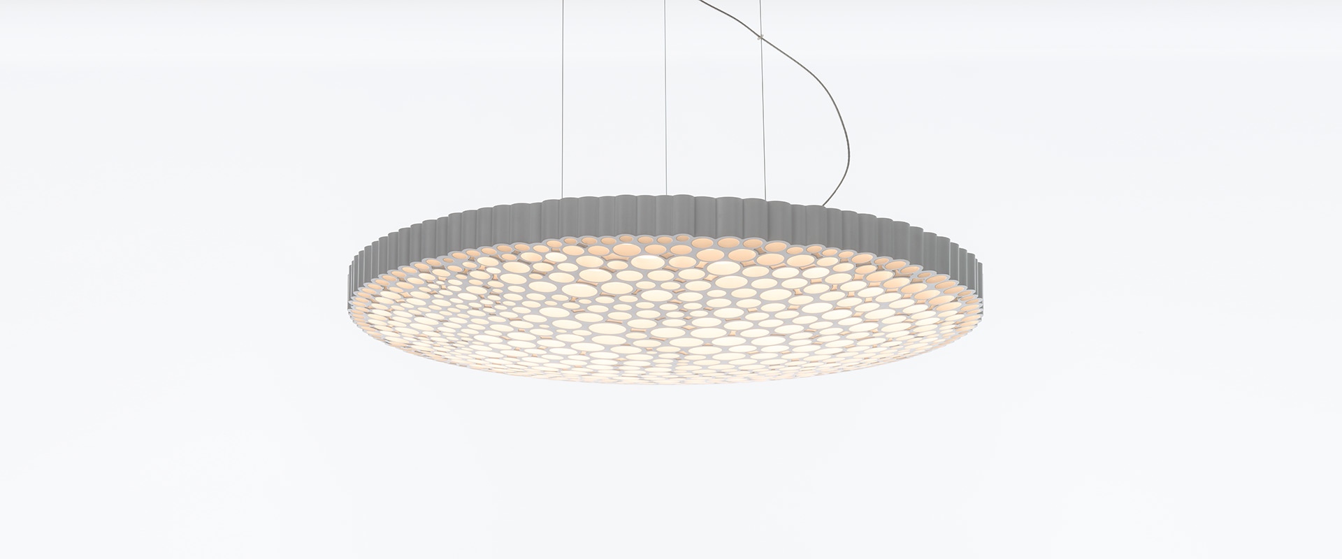 Artemide Calipso suspension lamp: large circular pendant with honeycomb diffuser pattern, soft white glow, suspended by thin cables