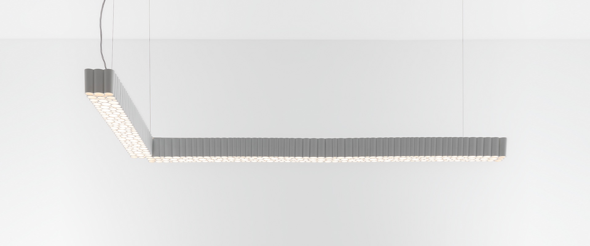 Artemide Calipso Linear System: L-shaped pendant lamp in grey with circular LED diffusers creating a honeycomb pattern, suspended from ceiling