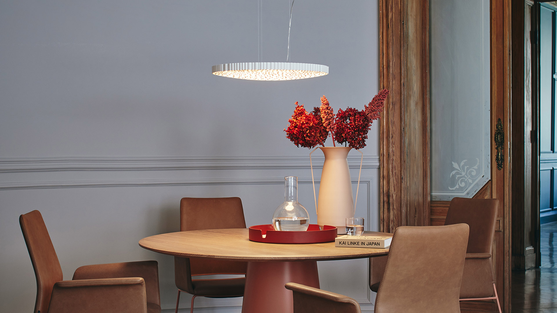 Calipso pendant lamp by Artemide, circular LED ring with crystal rods, suspended over a round dining table with chairs and floral arrangement