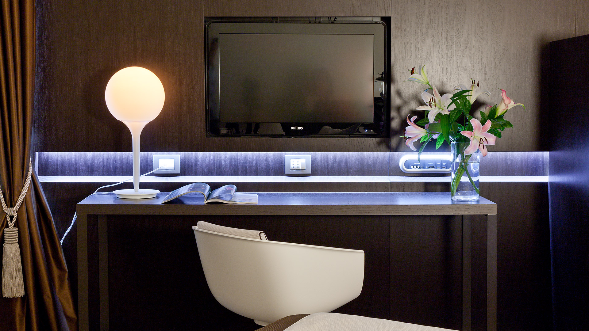 Artemide Castore table lamp with white spherical glass shade on a modern hotel desk, accented by blue LED strip lighting