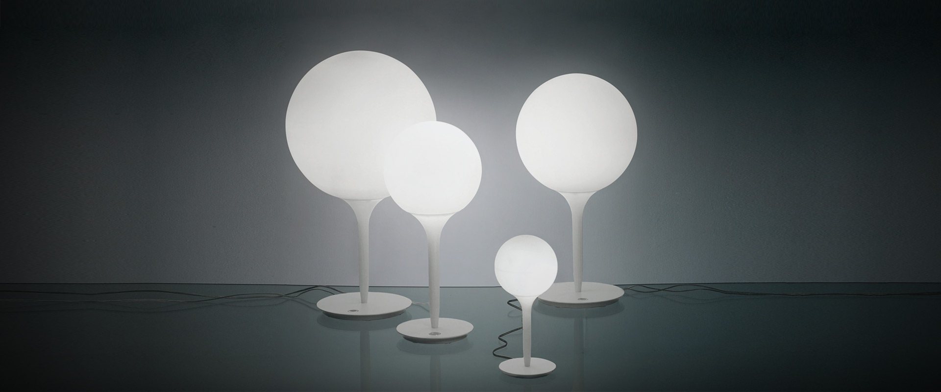 Four Artemide Castore Tavolo table lamps with white opal glass spheres in varying sizes on slender white stems and round bases
