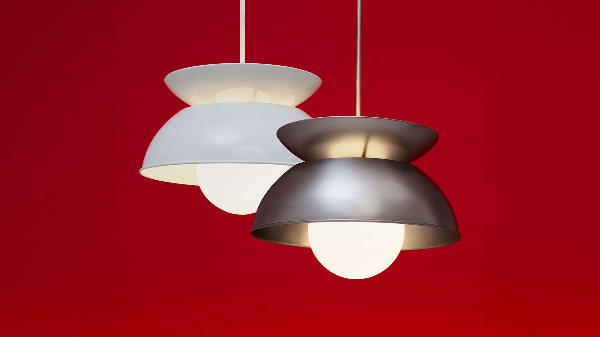 Two Artemide Cetra pendant lamps: white and gray versions, each with double-disc shade and opal globe bulb, on red background