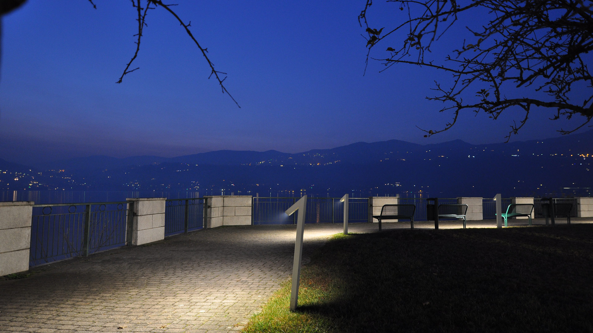Garden path at night lined with Artemide Chilone spike spotlights casting warm pools of light on grass between trees
