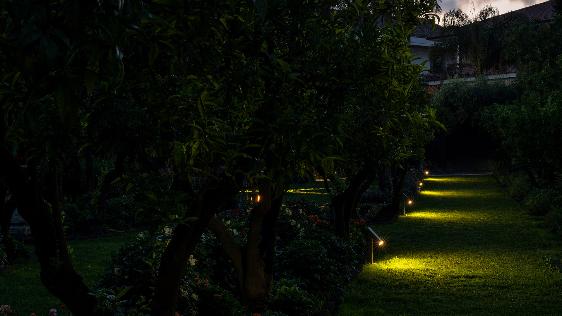 Row of Artemide Chilone floor lamps with angular white frames emitting warm orange light on a wooden deck at dusk
