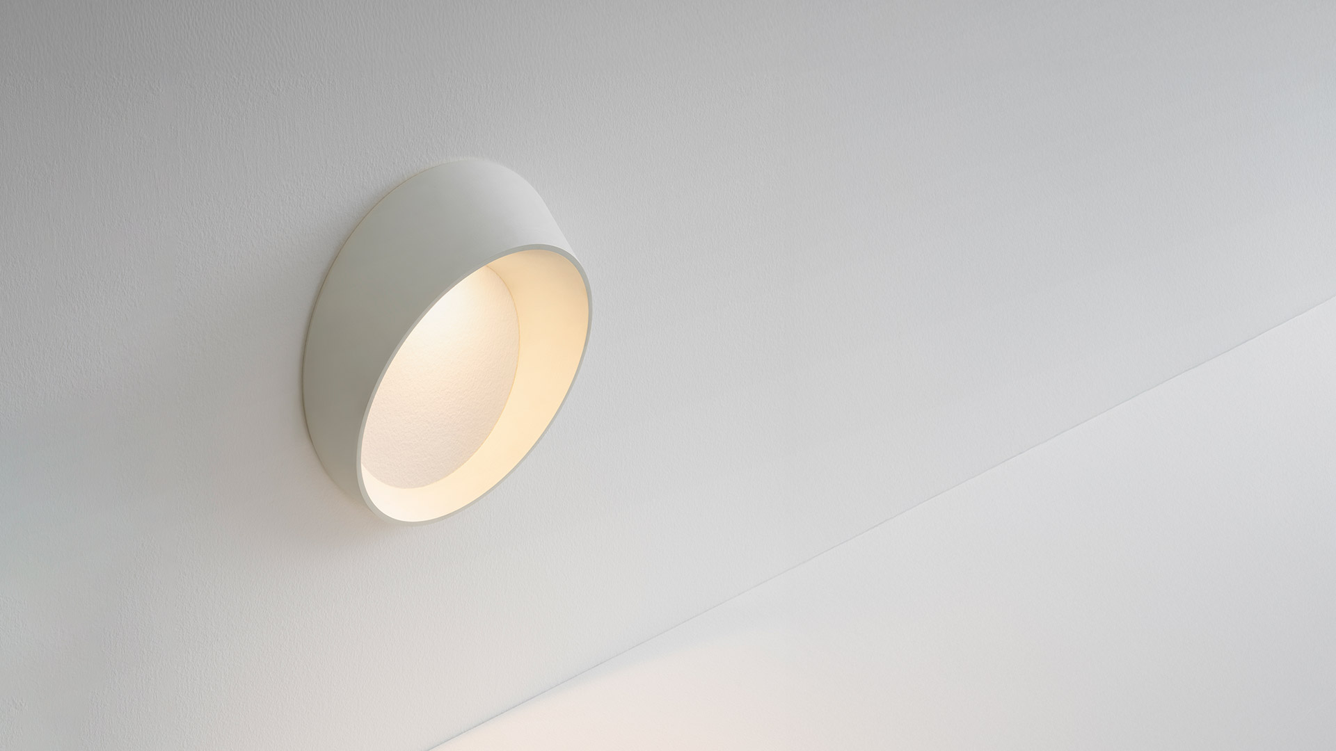 Artemide Cleomede wall sconce: white circular disc-shaped fixture with angled bowl emitting warm diffused light