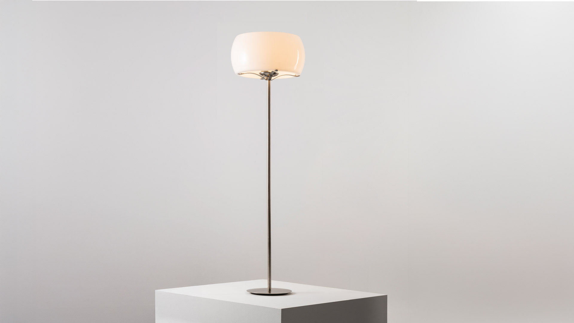 Artemide Clitunno floor lamp with opal white glass shade, decorative metal crown detail, and slim bronze stem on round base