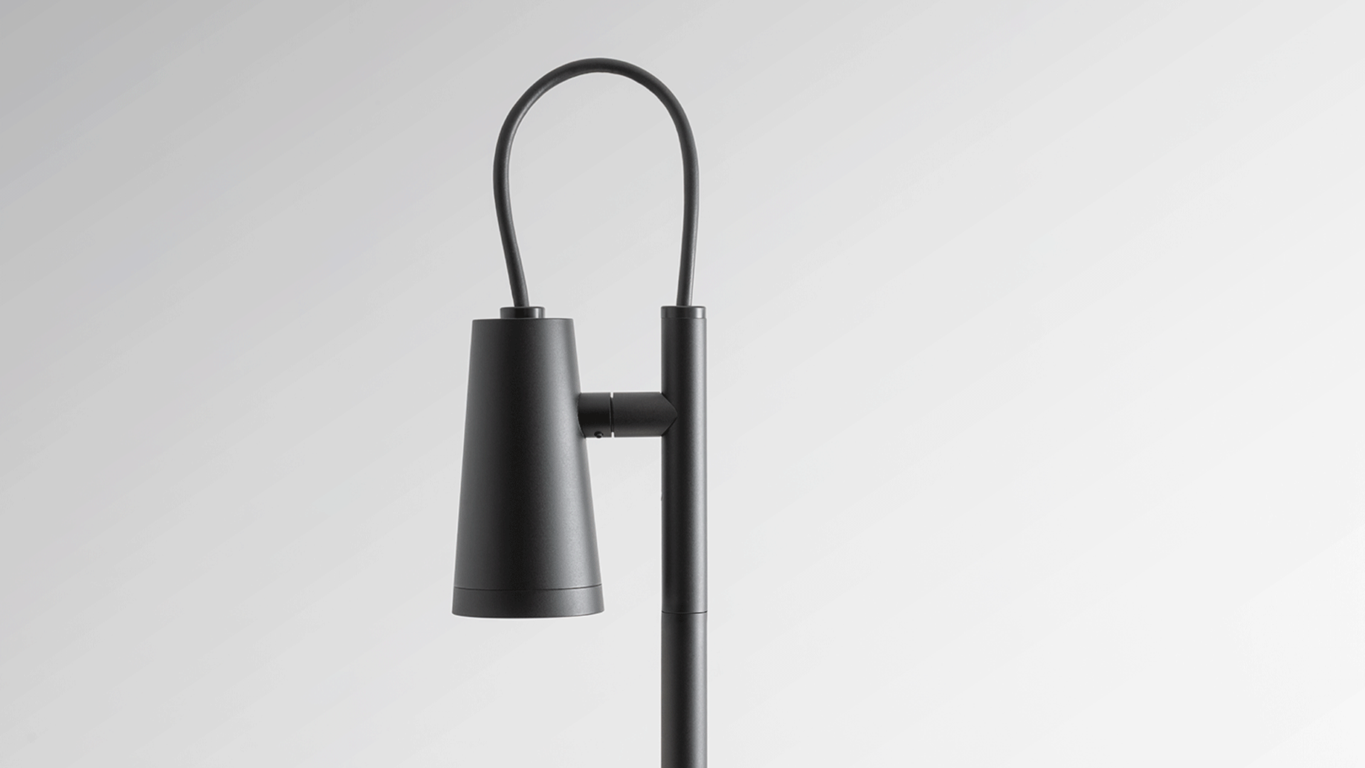 Artemide Conus outdoor bollard light in black, with adjustable cylindrical head, installed in a garden pathway among wild grass