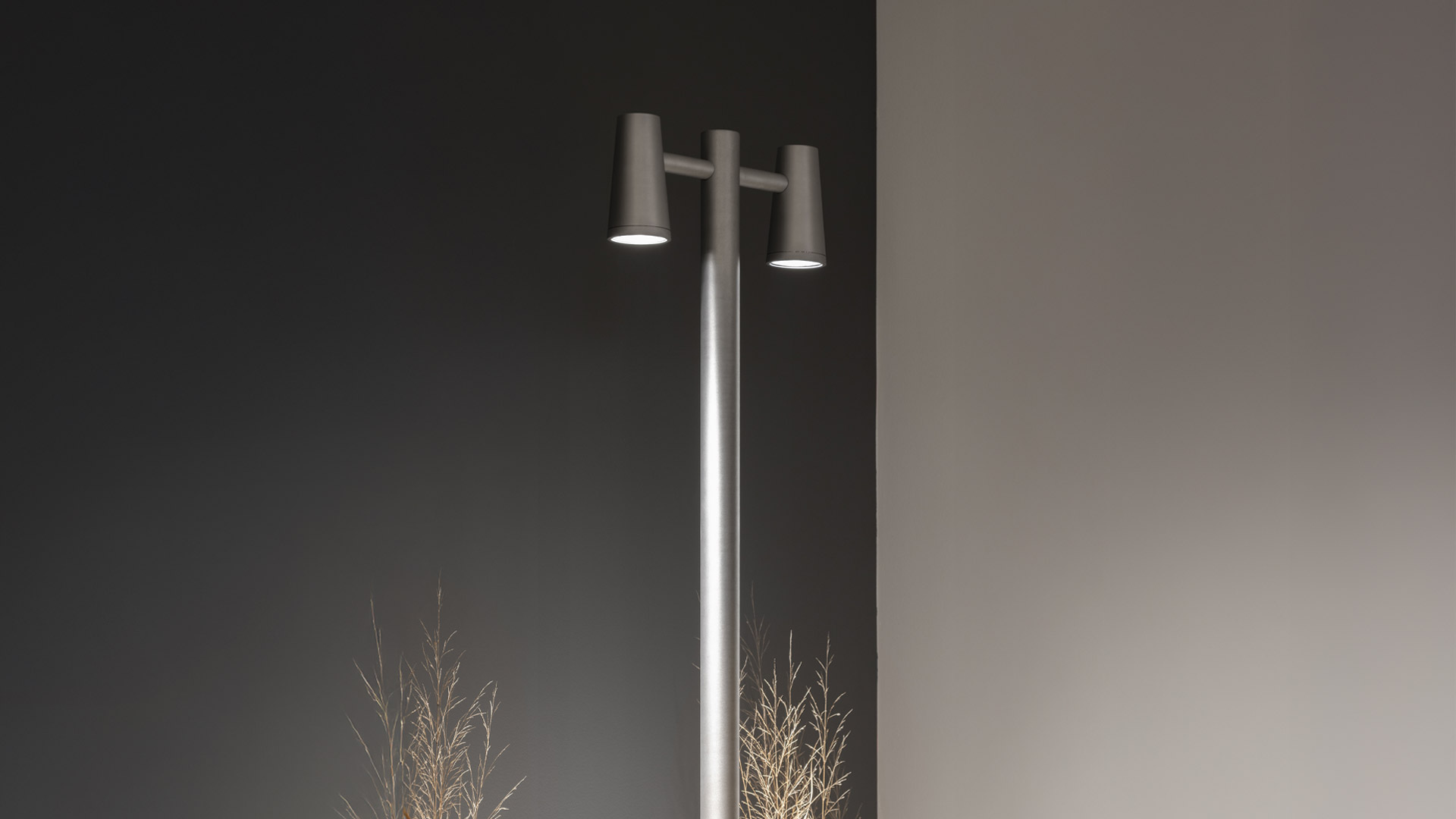 Artemide Conus outdoor spike spotlight in black, installed among lush garden grasses and shrubs, directing light downward