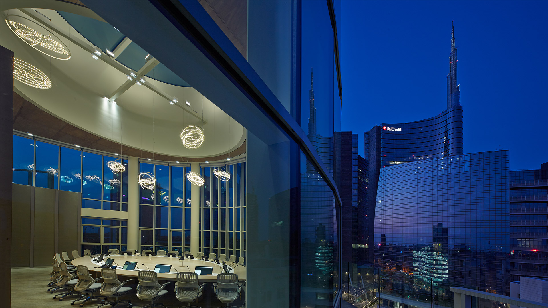 Elegant boardroom with Artemide Copernico suspension lamps over oval table, floor-to-ceiling windows revealing city skyline at dusk