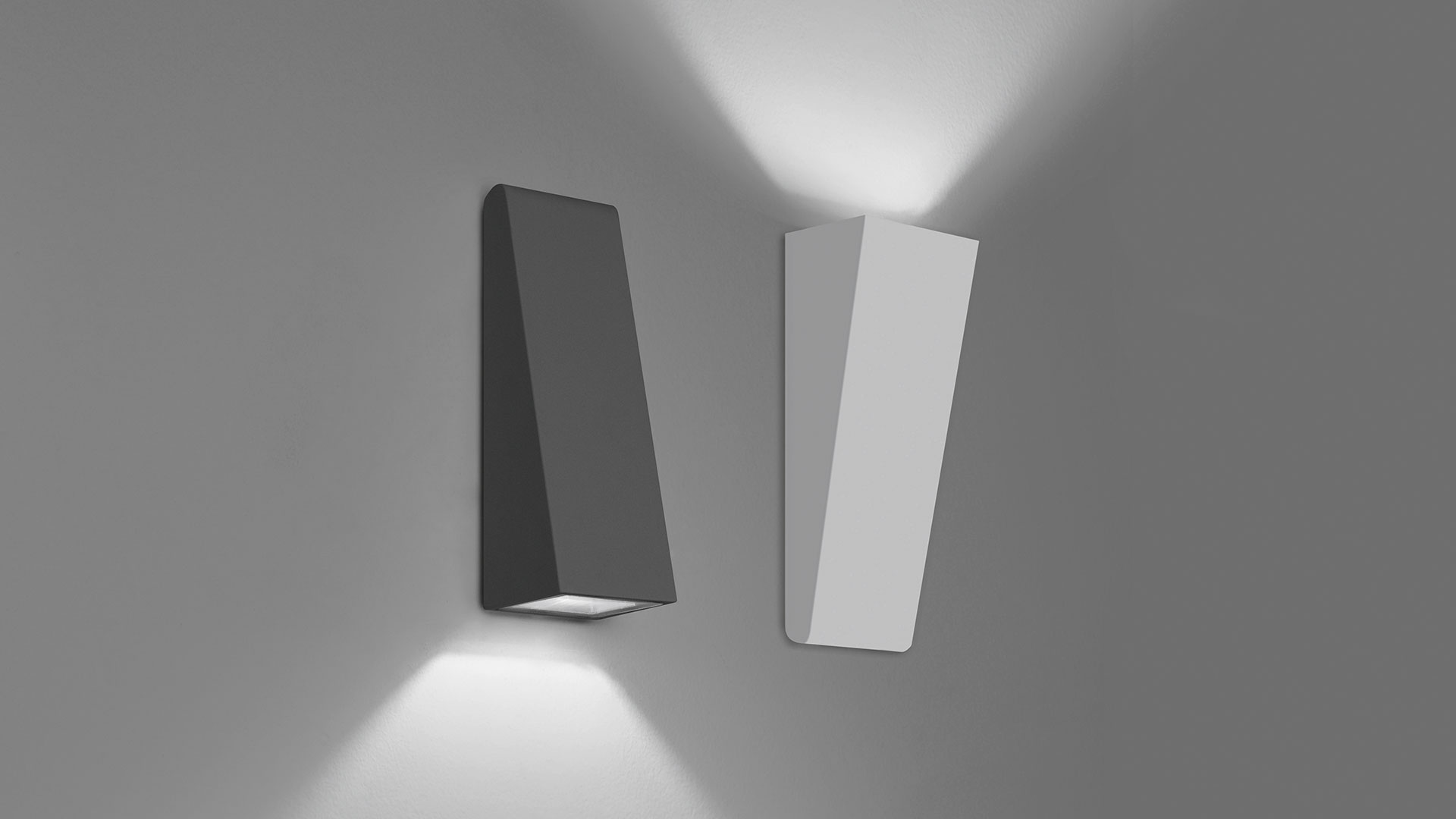 Two Artemide Cuneo dark wall lights mounted on a stone wall, casting warm downward beams, surrounded by lush green foliage at night