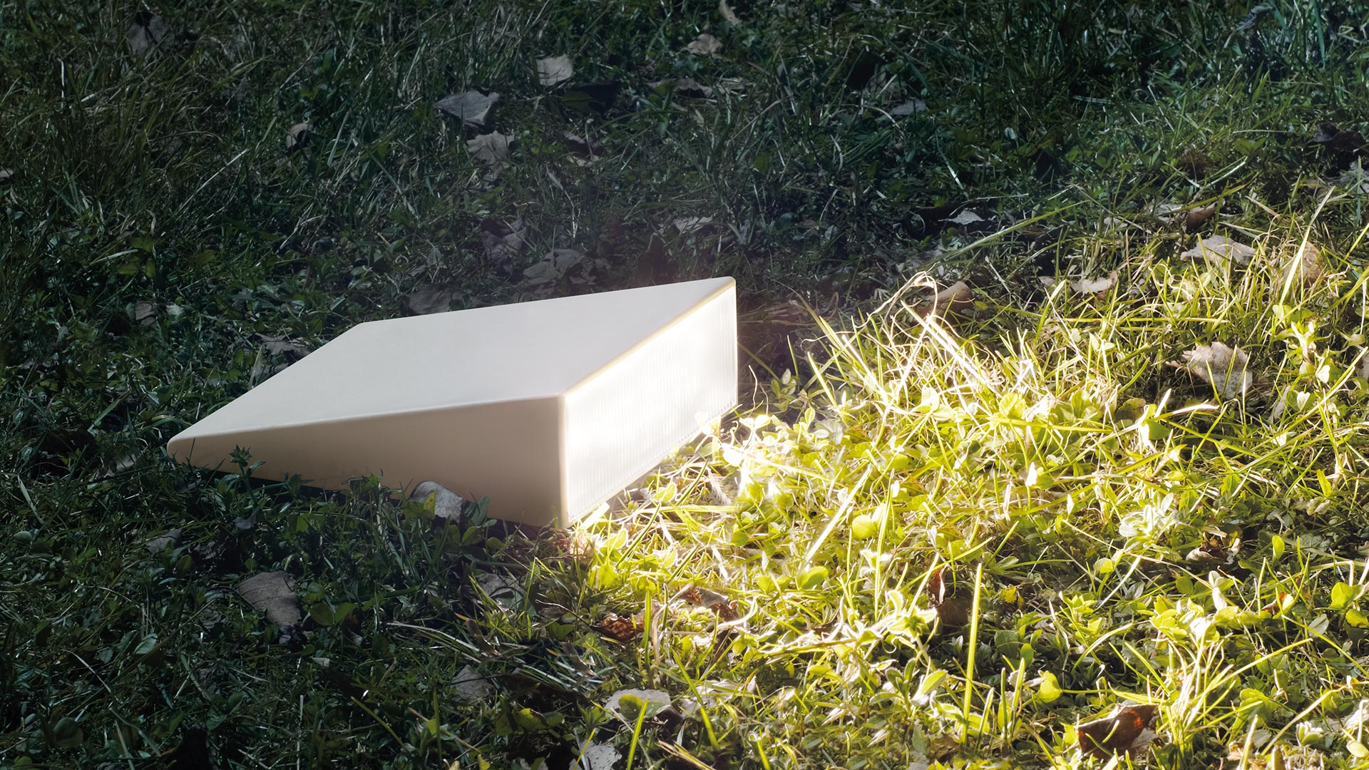 Artemide Cuneo wall-mounted outdoor lights on a brick garden wall, casting warm downward glow onto a brick pathway at night