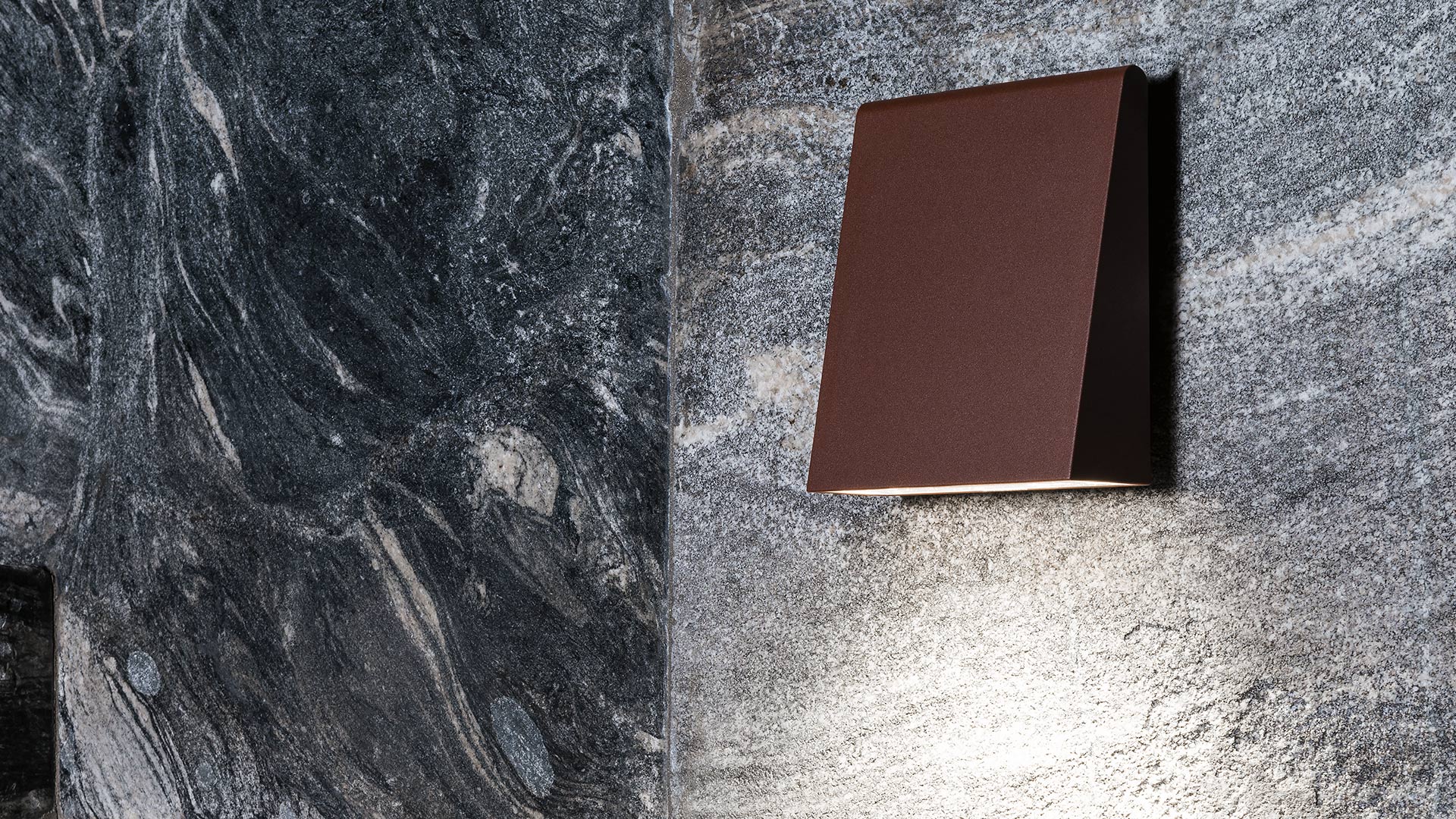 Artemide Cuneo wall lamp in dark red finish, mounted on marble wall, emitting downward light beam