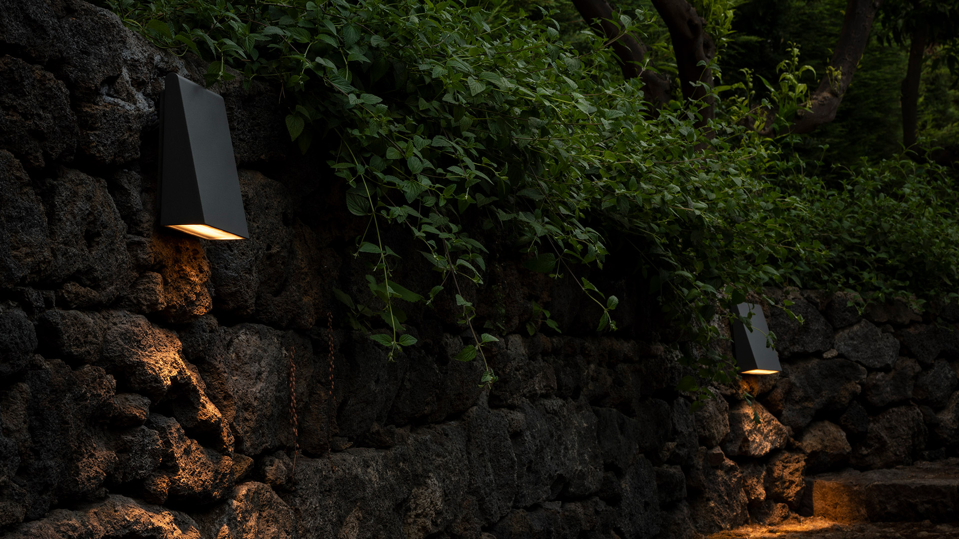 Two Artemide Cuneo wall sconces: dark and white trapezoidal fixtures emitting upward and downward light beams on a grey wall