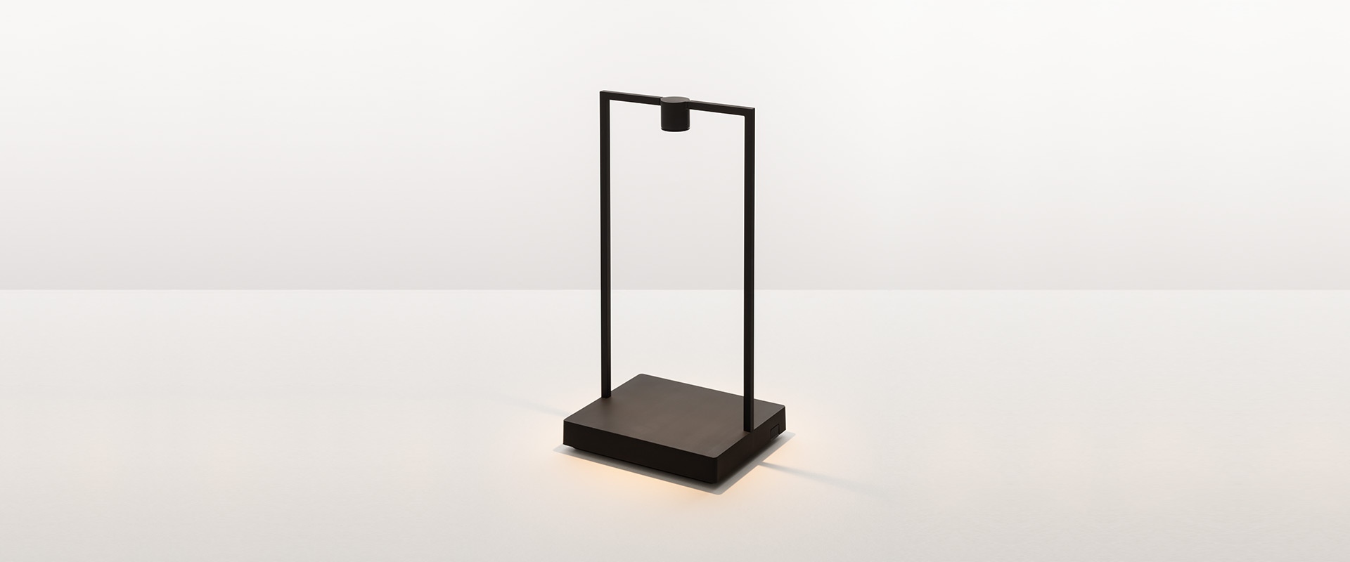 Artemide Curiosity table lamp with black rectangular frame and wooden base, doubling as a magazine holder on a white shelf