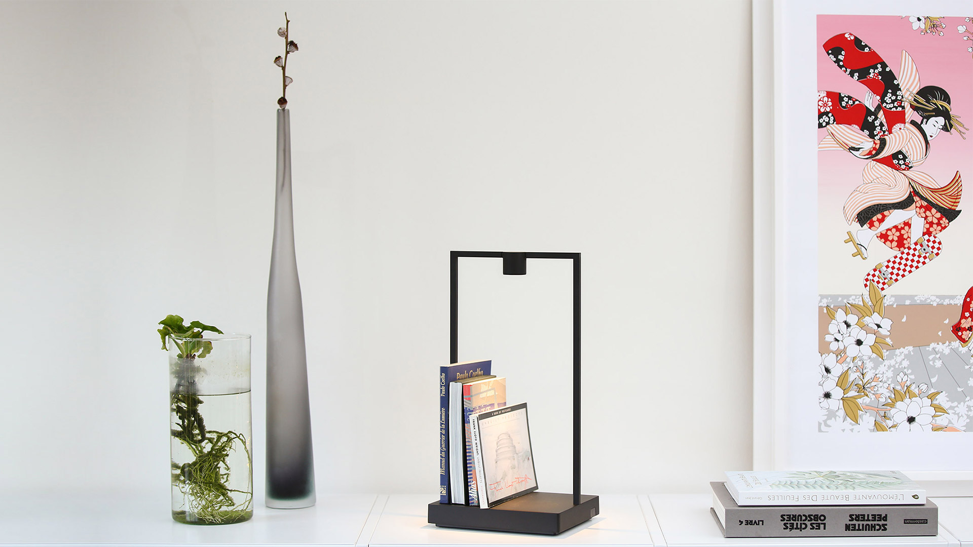 Artemide Curiosity table lamp: black rectangular frame with warm LED base light illuminating gold and dark blue display objects