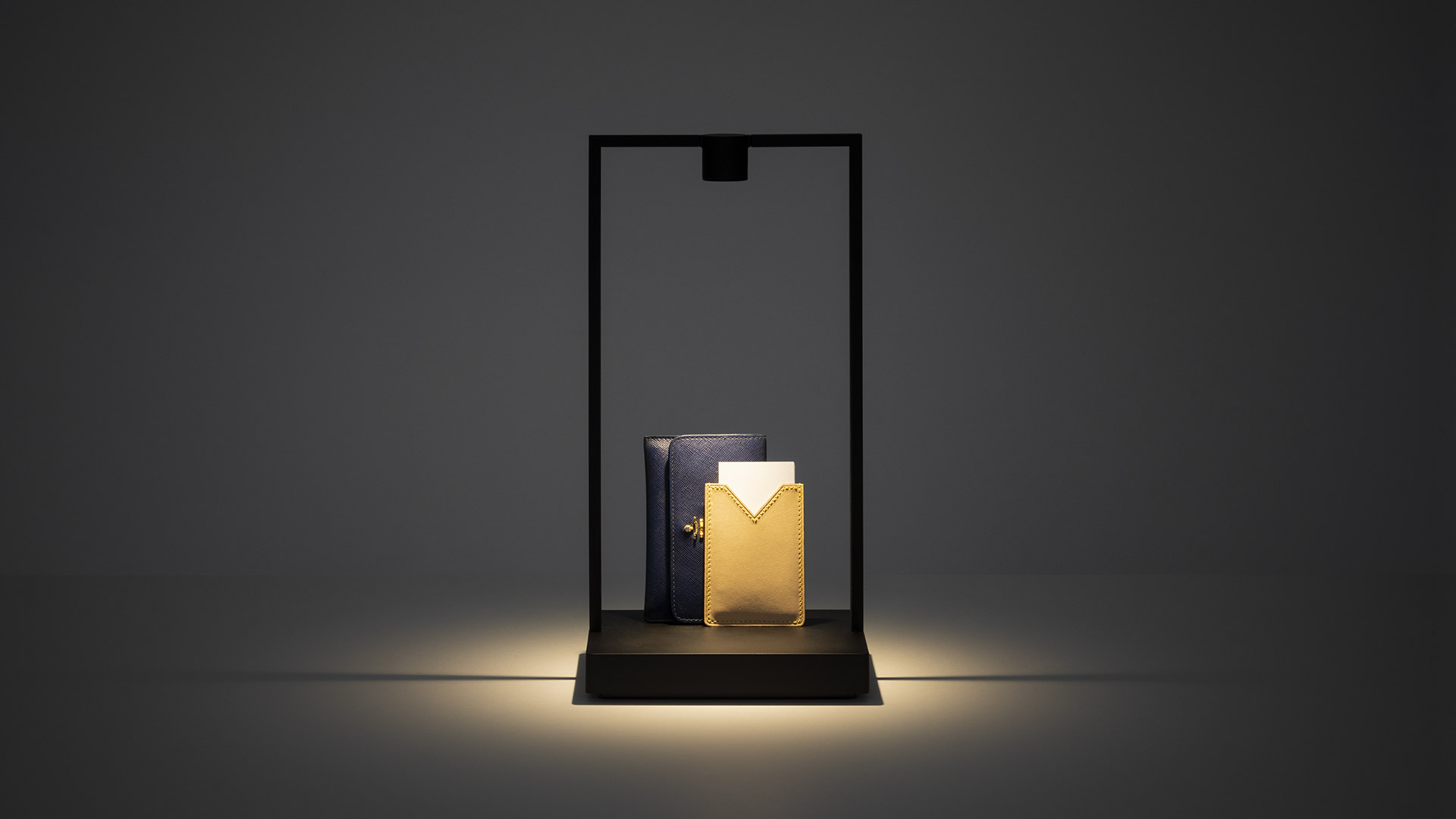 Three Artemide Curiosity table lamps with geometric black frames on a white surface, beside colorful abstract artwork on the wall