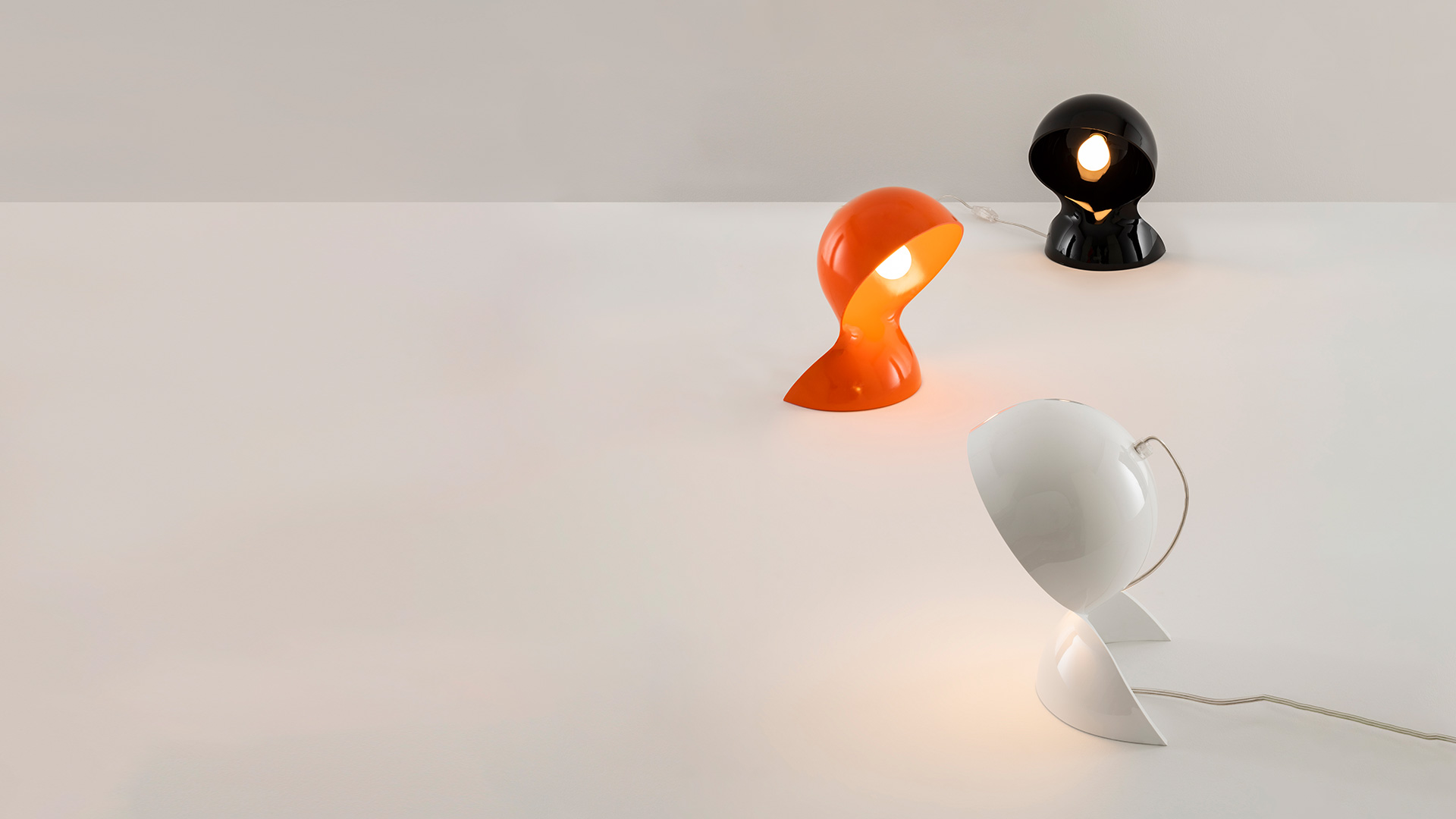 Artemide Dalù table lamp in orange, displayed on a red stepped pedestal against deep red velvet curtains on a theater stage