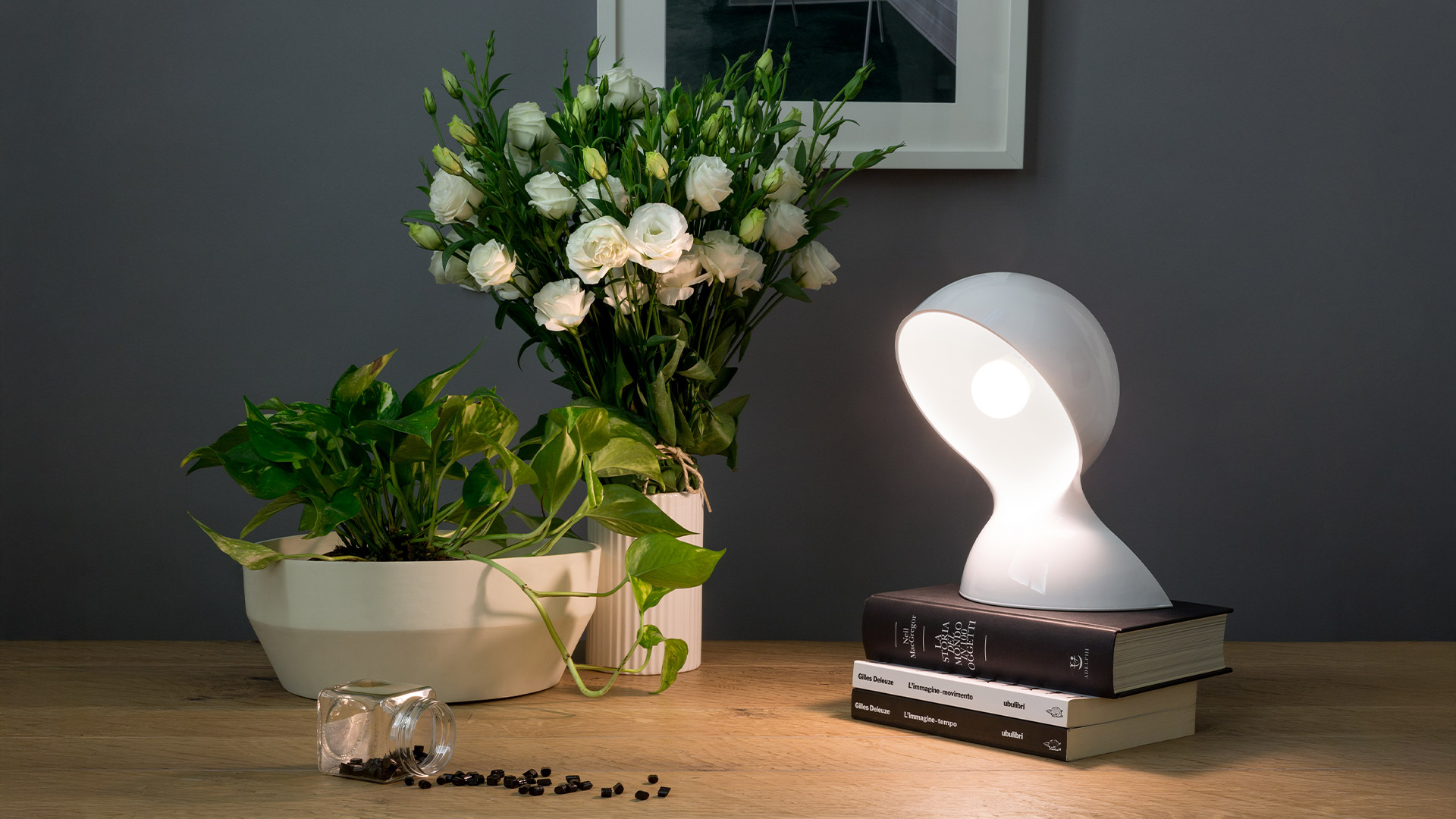 Two Artemide Dalù table lamps in purple and yellow with round bulb heads, beside a tall white architectural tower structure on a white table