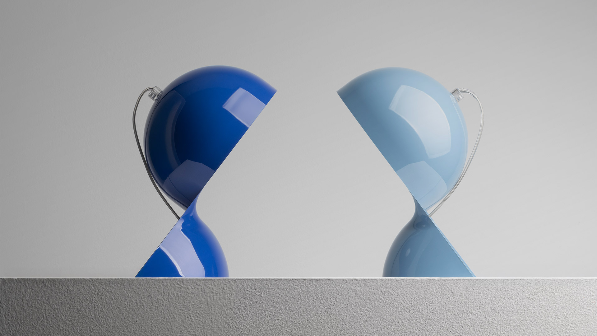 Two Artemide Dalù table lamps facing each other: left in deep blue, right in light blue, both with glossy spherical shades tilted downward