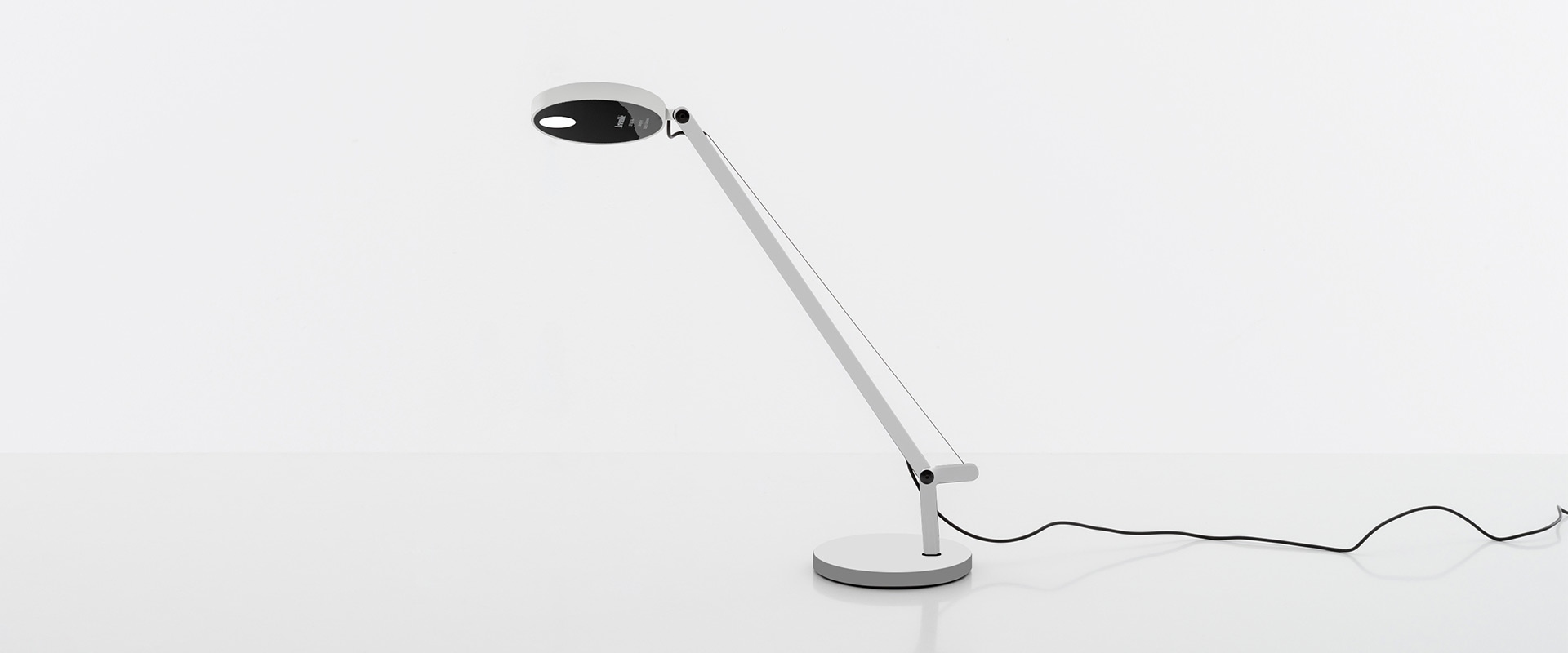 Artemide Demetra Micro table lamp in white on a desk with plants, cacti, and geometric artwork in a minimalist white interior