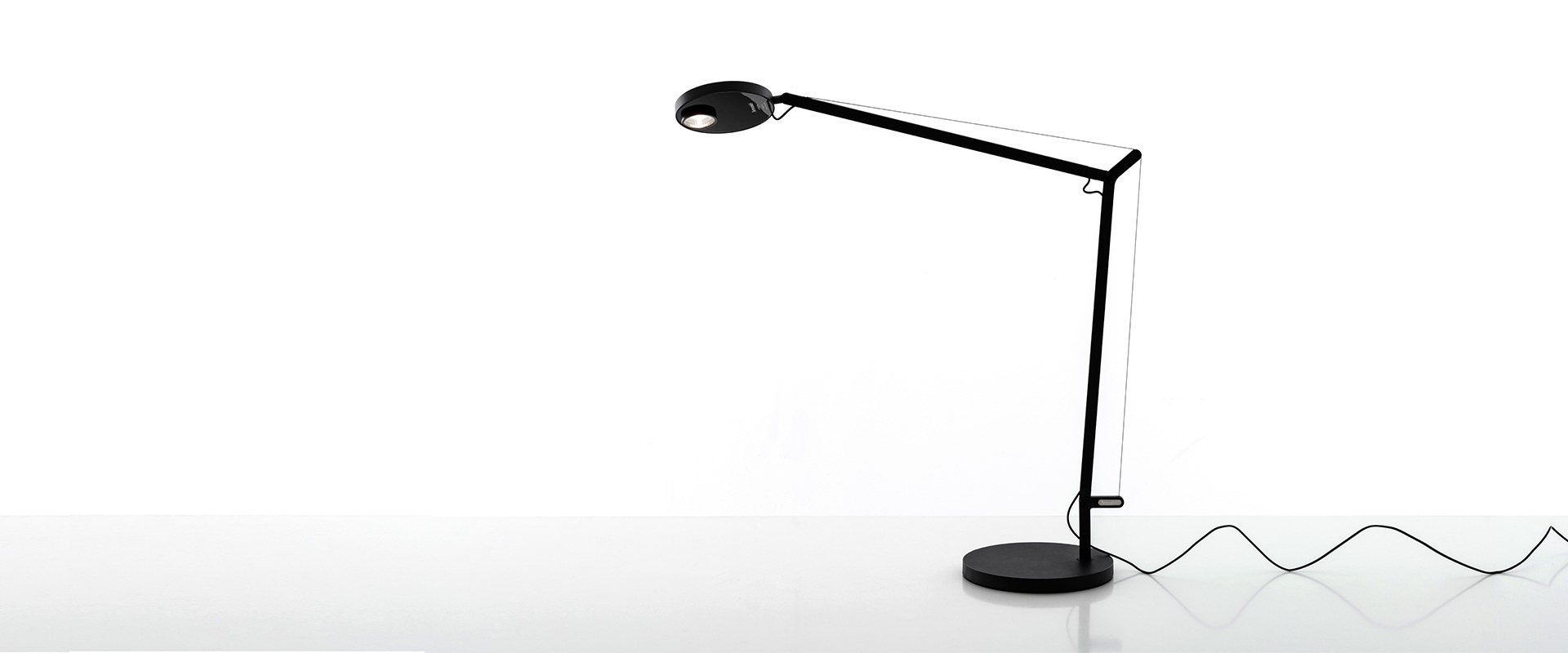 Artemide Demetra Professional table lamp in black, featuring an adjustable articulated arm, circular LED head, and round base with power cord.