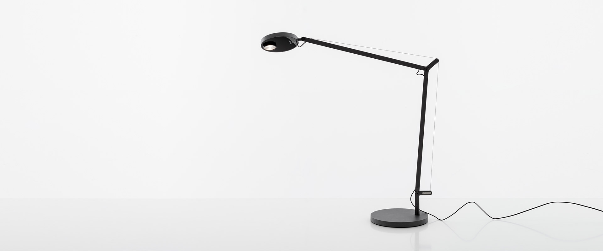 Artemide Demetra Professional table lamp in black, featuring an adjustable arm, circular LED head, and round weighted base.