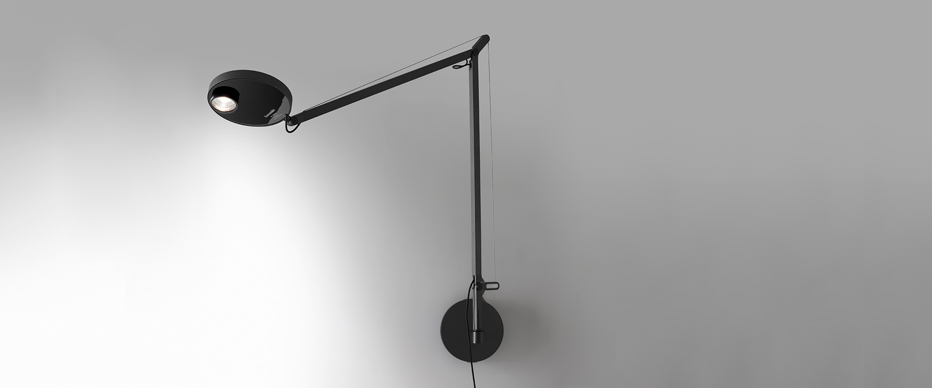 Artemide Demetra wall lamp in black, featuring an adjustable arm, circular head with LED light, and round wall-mount base.