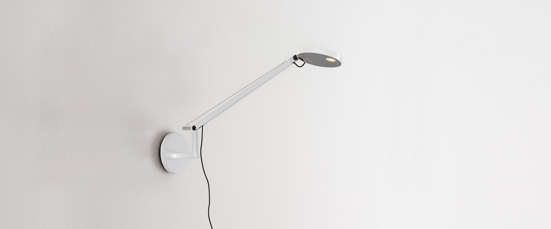 Artemide Demetra Micro wall lamp in black, featuring a slim adjustable arm and circular LED head mounted on a round wall base