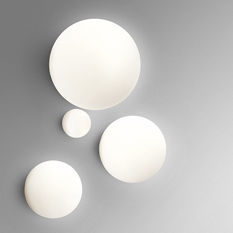 Four Artemide Dioscuri wall/ceiling lamps in different sizes, featuring opal white spherical diffusers mounted on a grey wall