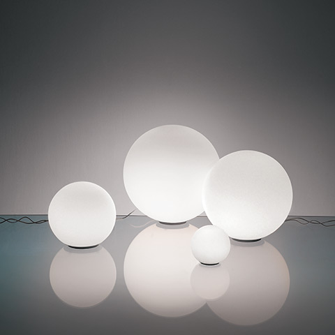 Four Artemide Dioscuri table lamps in frosted white glass spheres on small black bases, displayed in four sizes on a reflective surface