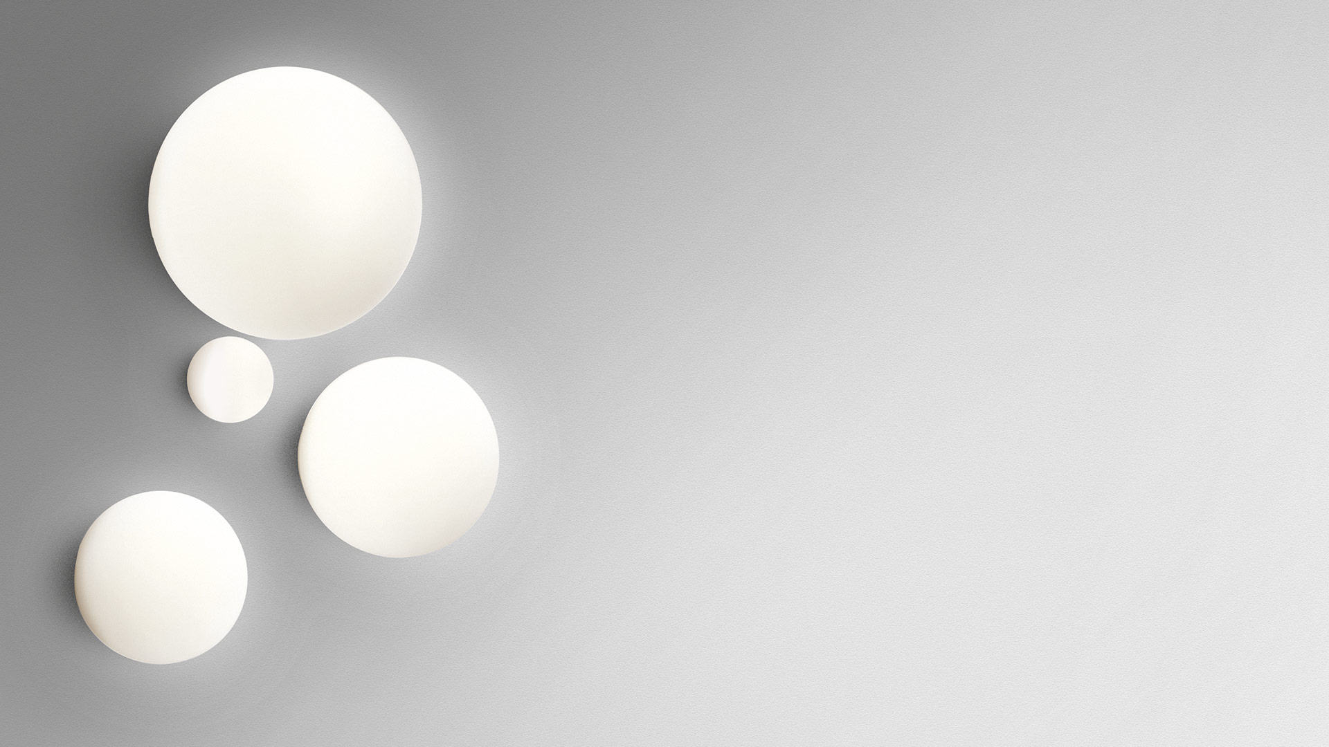 Three Artemide Dioscuri wall/ceiling lamps in different sizes, opal white spherical diffusers mounted on a grey wall