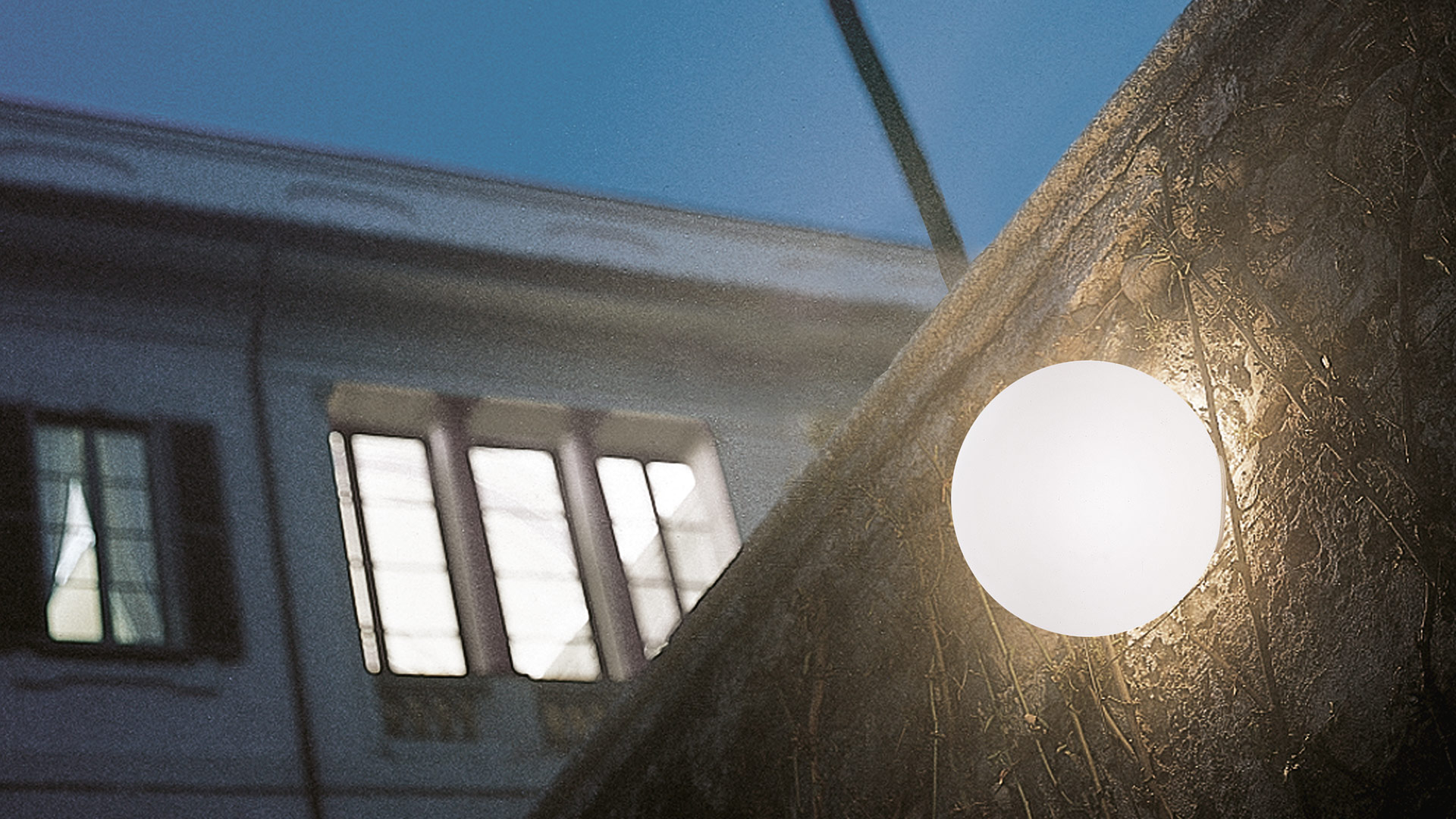 Artemide Dioscuri wall/ceiling lamp with opal glass diffuser mounted on textured stone surface, classical building reflected in background