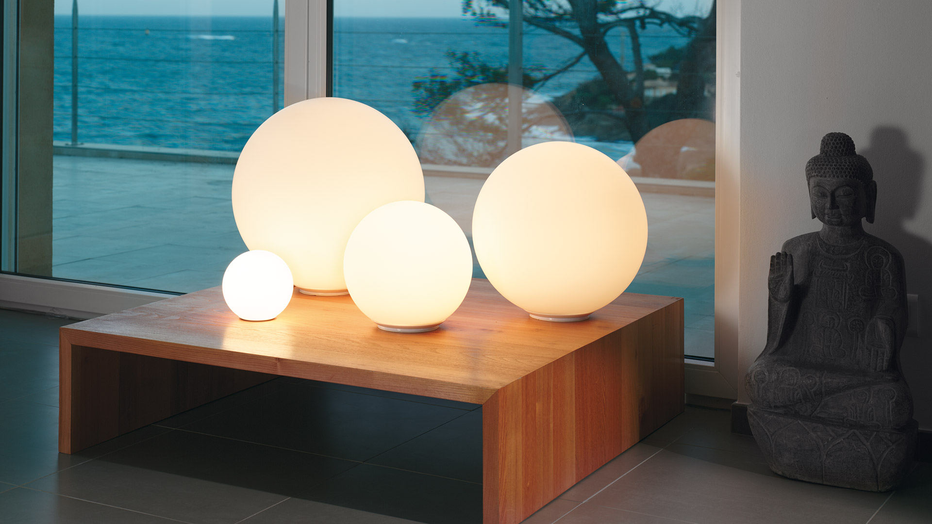 Four Artemide Dioscuri table lamps in opal white glass spheres of varying sizes arranged on a white surface against a warm yellow wall