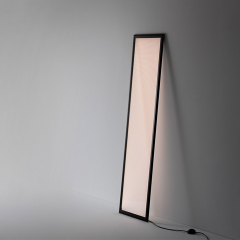Artemide Discovery Terra floor lamp: tall rectangular luminous panel with black frame, leaning against a wall, emitting warm diffused light