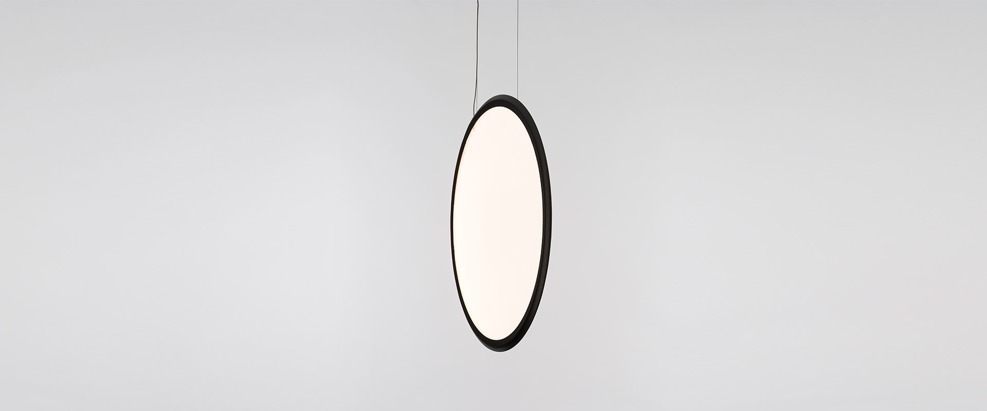 Elegant dining room with a large circular Artemide Discovery pendant lamp as a luminous focal point above a rustic wooden table.