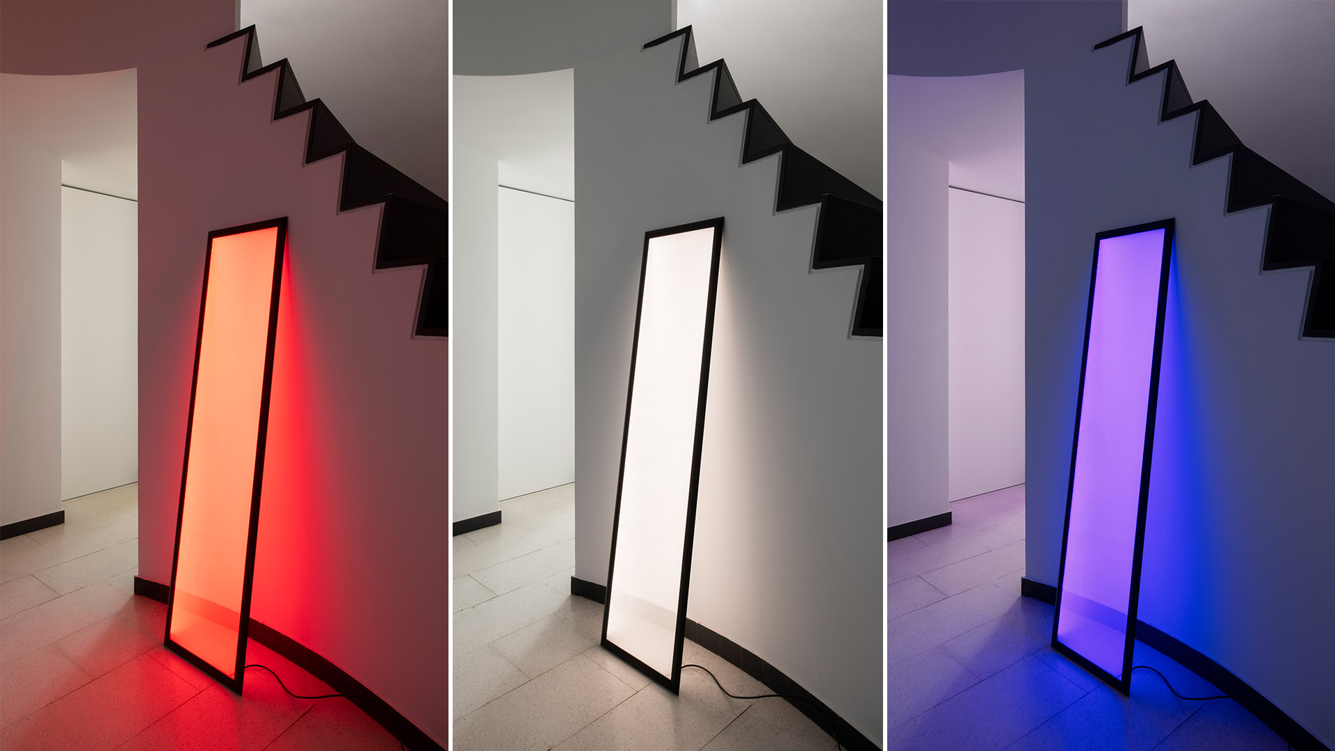 Artemide Discovery Terra floor lamp: tall rectangular LED panel with black frame, leaning against wall, emitting warm diffused light