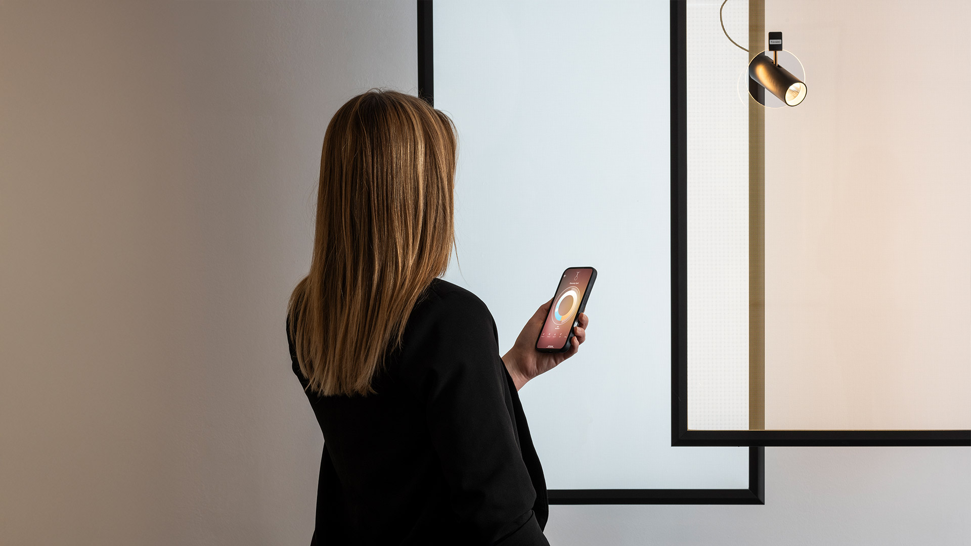 Artemide Discovery Spot: black pendant spotlight with cylindrical head inside a thin circular ring, suspended by a cable against a mesh panel