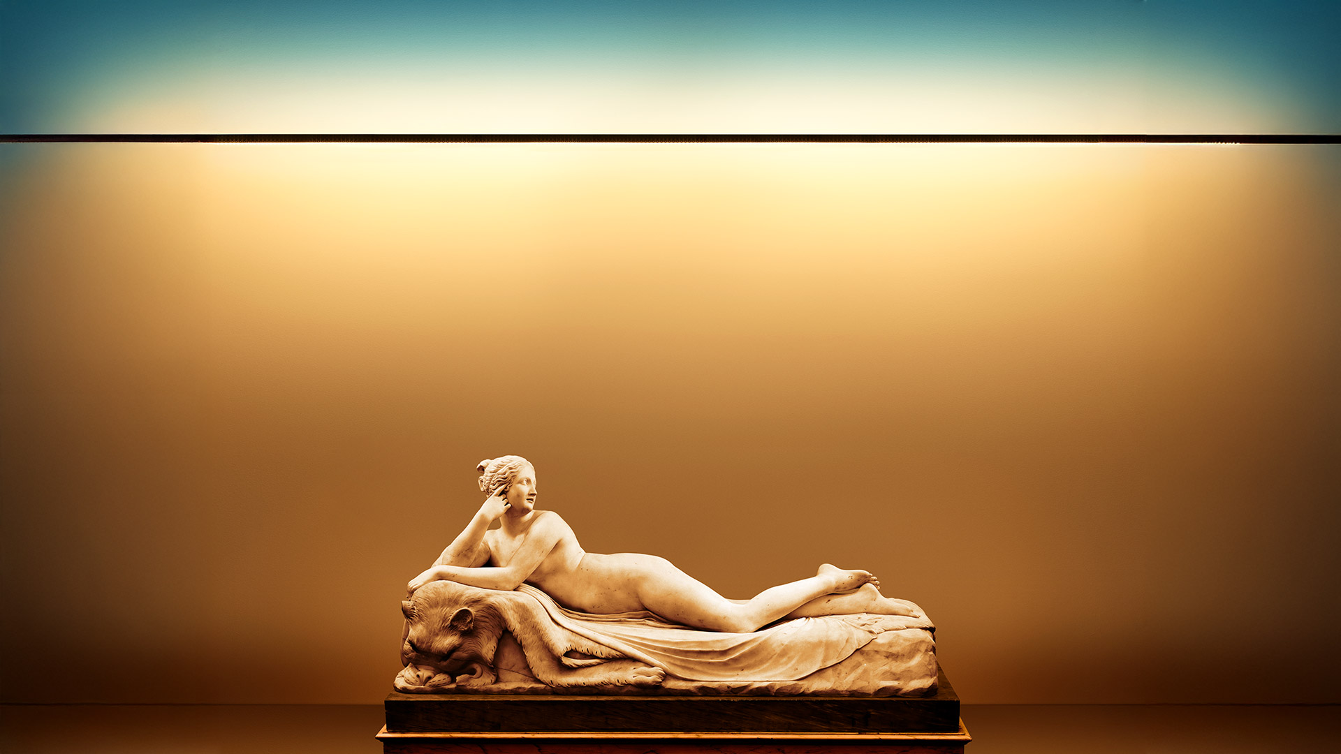 Classical reclining marble sculpture dramatically illuminated by Artemide Dusk linear LED light, casting warm golden glow on museum wall