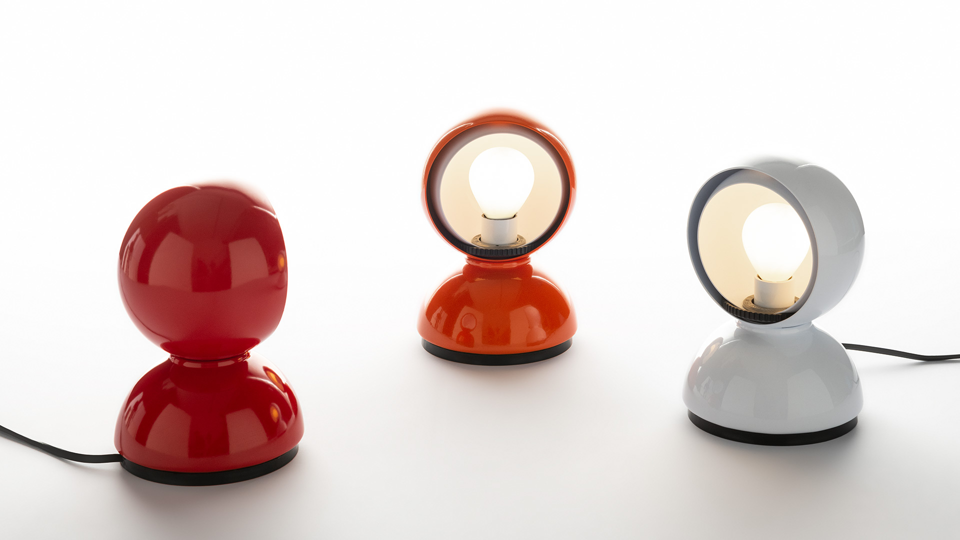 Four Artemide Eclisse table lamps in gold, copper, chrome, and black finishes, each with a rotatable spherical shade revealing the bulb