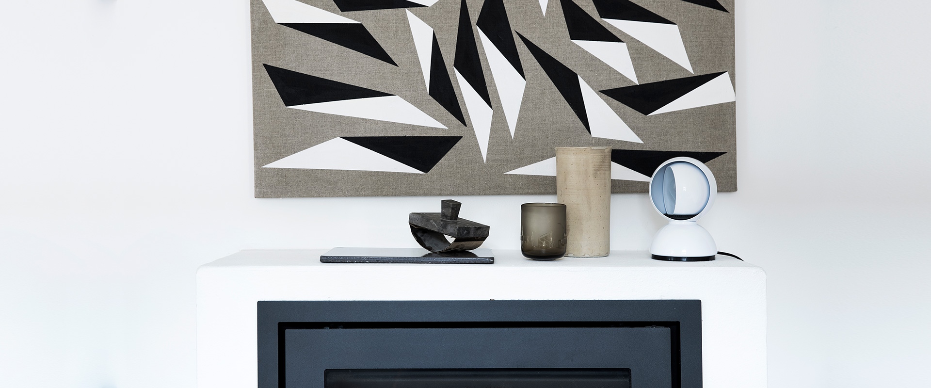 White shelf with decorative objects and an Artemide Eclisse table lamp in white, against a geometric black and white artwork