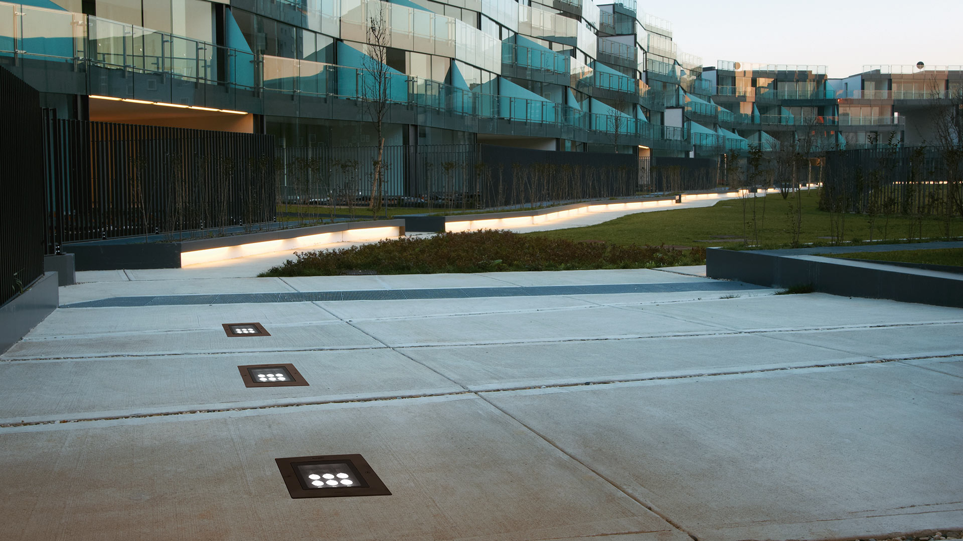 Modern building exterior at dusk with Artemide Ego 220 flat walk-over lights illuminating columns and landscaped lawn