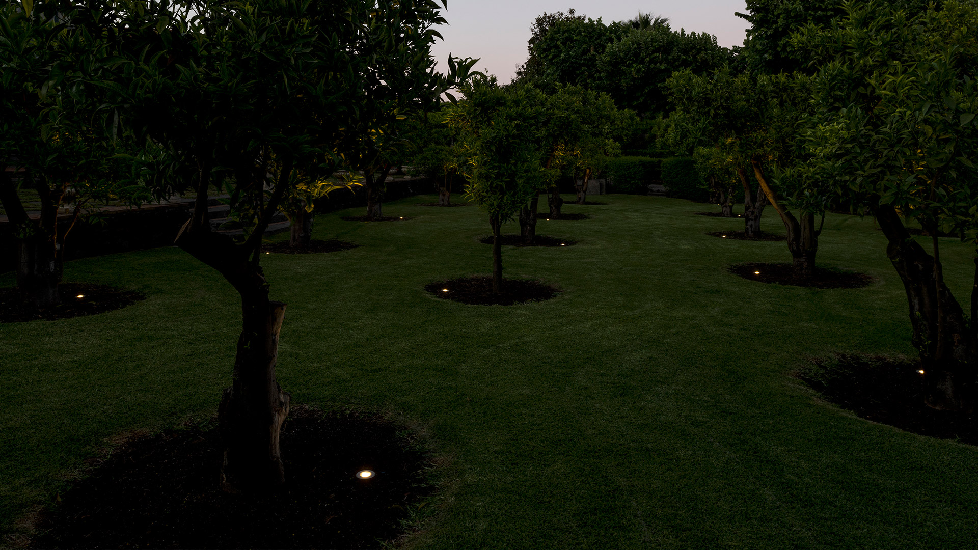 Artemide Ego 90 downlight recessed in gravel ground, circular dark metal frame with warm white LED light facing upward