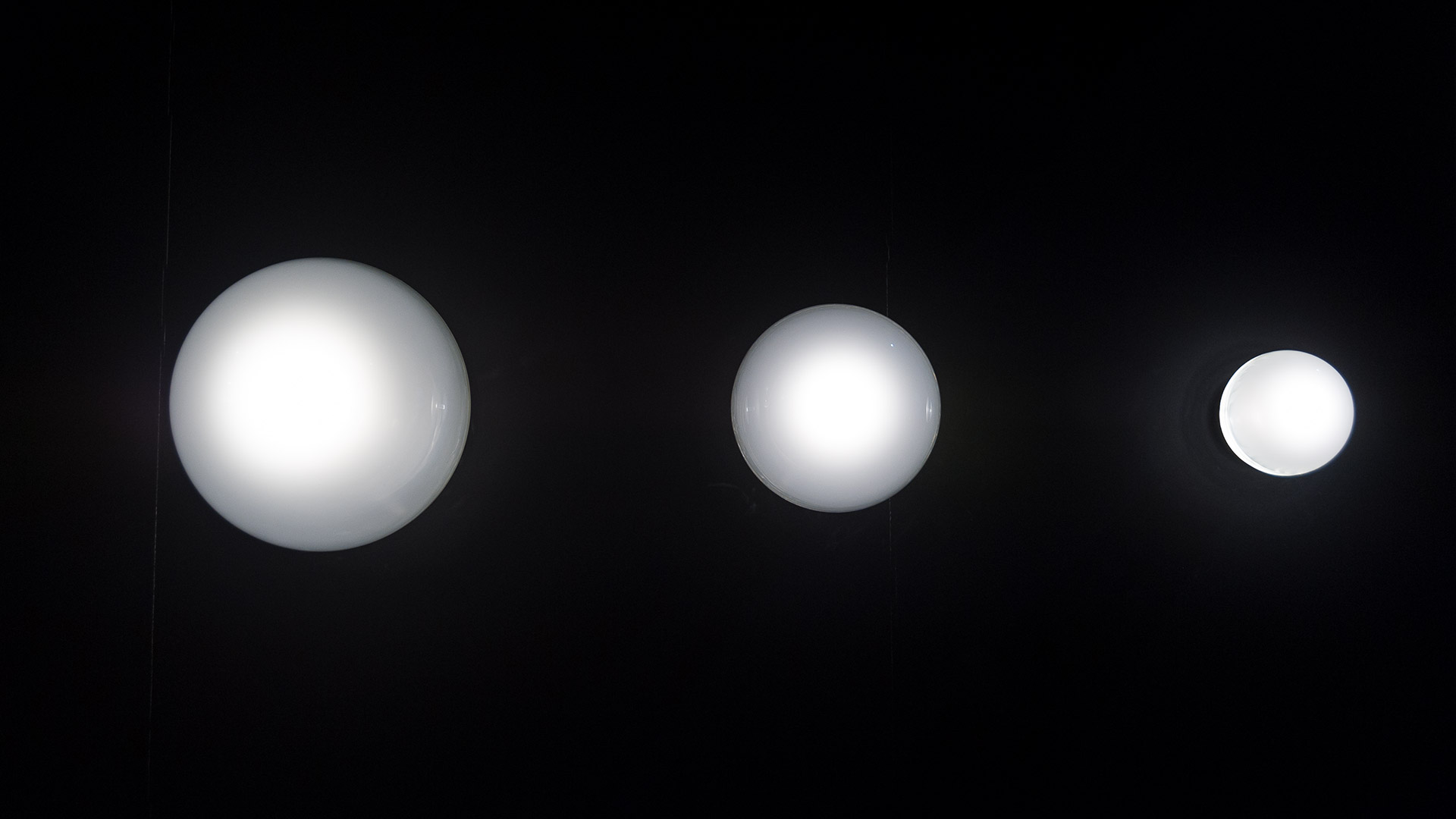 Three Artemide Empatia wall/ceiling lights in different sizes, with transparent glass domes and central LED elements mounted on a dark ceiling
