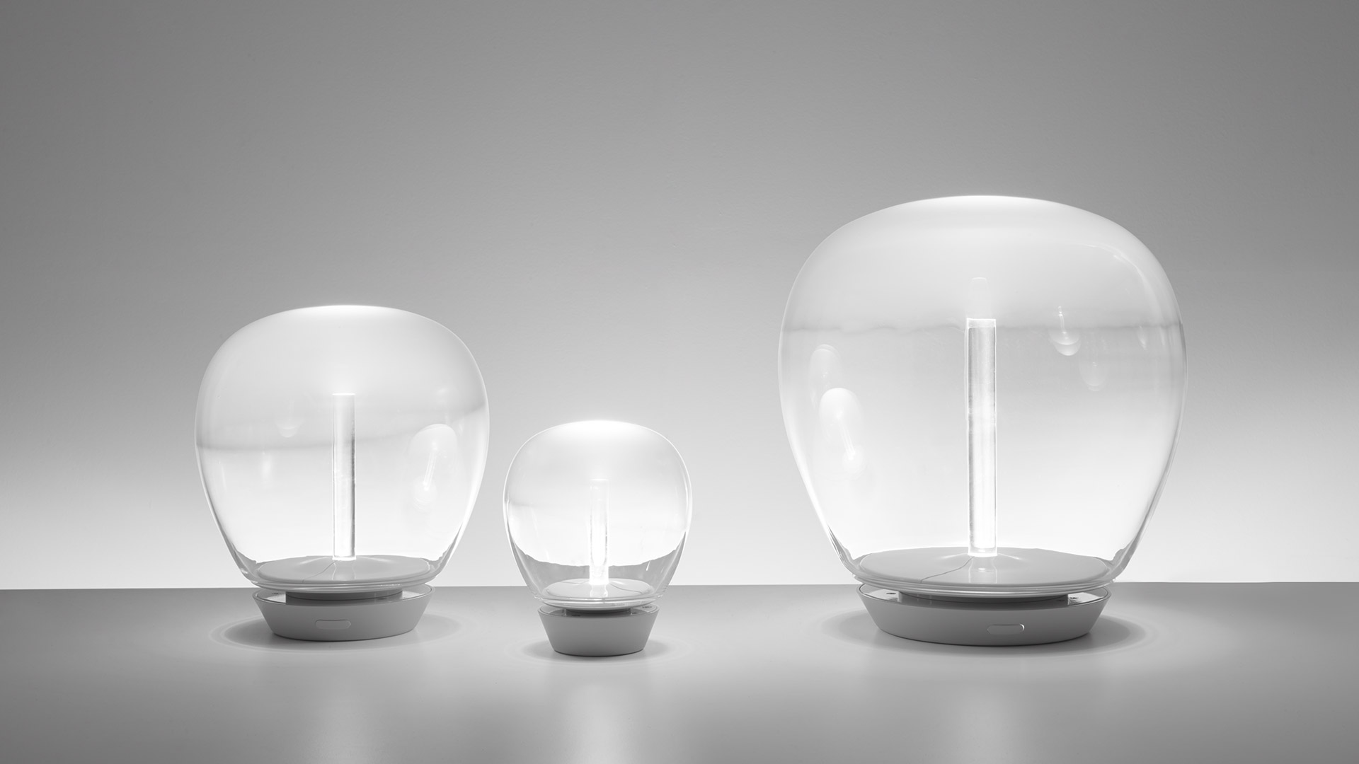 Artemide Empatia table lamp: hands touching a glowing spherical transparent glass diffuser with central LED stem on white base